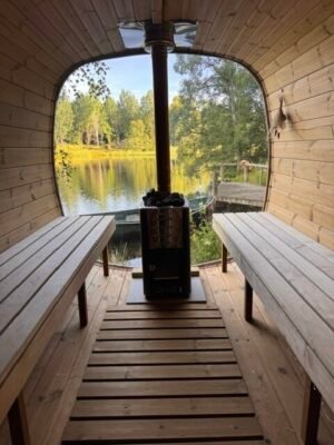 Interno della sauna mobile TimberIN Nordic Square con panche in legno e stufa a legna accanto a un lago