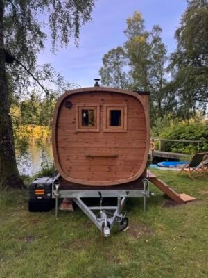 Vista frontale della sauna mobile TimberIN Nordic Square su rimorchio accanto a un lago