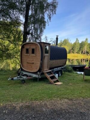 Vista laterale della sauna mobile TimberIN Nordic Square su rimorchio con camino accanto a un lago