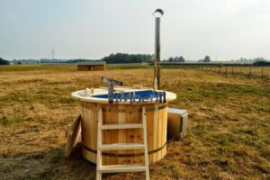 TimberIN Nordic Flex vista frontale su un prato, con vasca interna blu, scaletta in legno e parte del coperchio appoggiata a sinistra