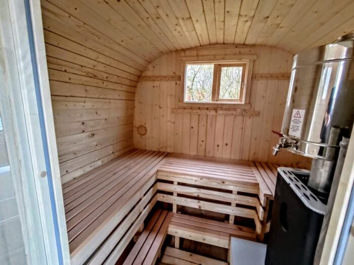 Interno di una sauna da esterno con panche in legno chiaro e stufa