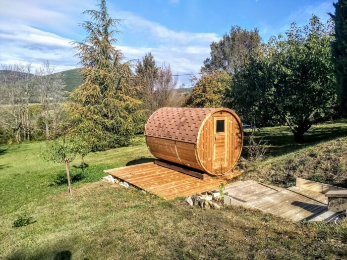 Sauna a botte appoggiata su una base in legno in un prato in pendenza