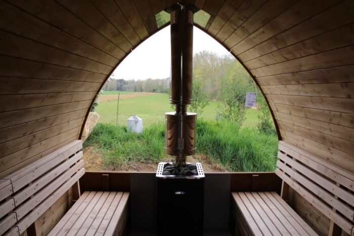 Interno di una sauna a igloo con stufa a legna tra le panche e vetrata sul prato