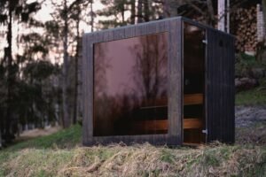 Sauna moderna TimberIN Nordic Cube con vetro scuro in mezzo al bosco