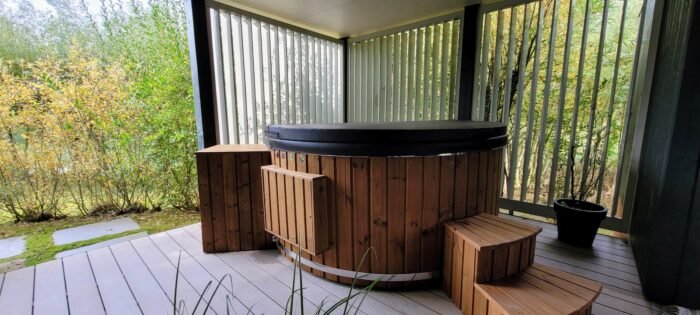 Vasca idromassaggio rotonda in legno con coperchio e vano tecnico laterale in legno, su una terrazza coperta senza camino