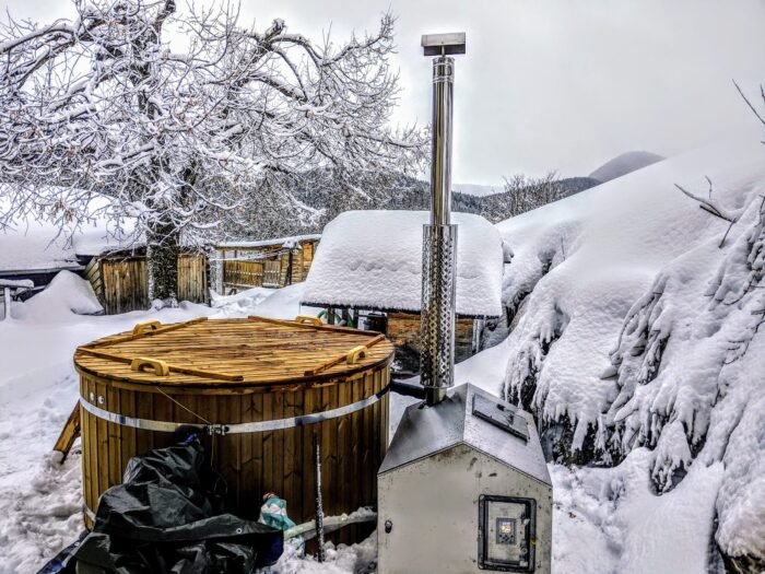 Vasca idromassaggio in legno con camino in un giardino coperto di neve
