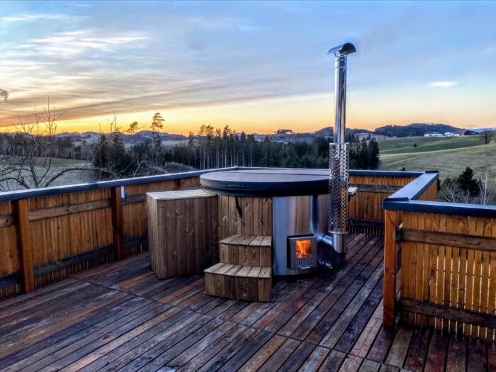 Vasca idromassaggio su una terrazza in legno con la stufa a legna accesa al tramonto