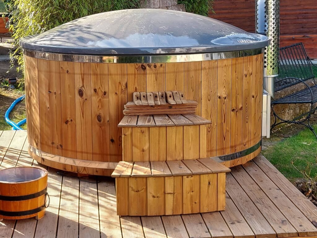 Vasca idromassaggio rotonda con rivestimento in legno termotrattato, coperchio e scaletta, su una pedana in legno